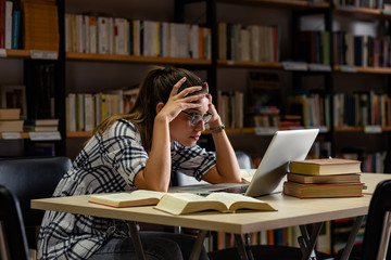 Exhausted female student study in the library using laptop for researching online.
