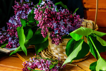 Basket with a branch of lilac flower on a wooden background