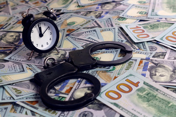 Alarm clock and handcuffs lie on a scattering of dollars. Concept - the time to combat financial...