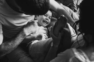 Close up portrait of a little smiling blond boy. He is playing with parents. Mother, father are sharing good emotions while relaxing at home Natural light, terracotta bed linen. Happy family at home.