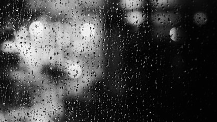 Window and rain drop in condominium or apartment room on a rainy day in Bangkok Thailand and background outside is blurred bokeh of raining city light and natural tree and sky.