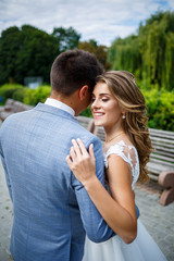 Obraz premium Young stylish guy in a suit the groom and the bride beautiful girl in a white dress with a train walk in the park on their wedding day