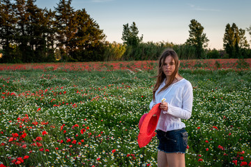 Young woman   in poppy feild., with  a red stra w hat ,relaxing ,provence France.