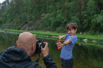 Sly and naughty little boy holding slingshot and posing for photographer outdoors. Close up...