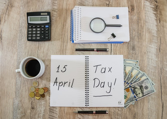 notepad with the inscription "TAX DAY April 15" and "tax day". View from above. Calculator, pen and cup of coffee on the table. Tax concept at office workplace.