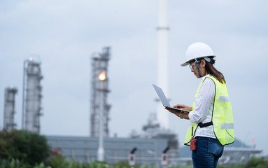 Shot of engineer woman wearing work helmet and reflective vest, checking data using laptop at power plant.