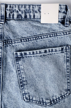 Vertical image of blue jeans and empty paper tag on it. Blank tag for price or clothing size