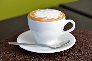 Cup of coffee with spoon on brown table with brown place setting
