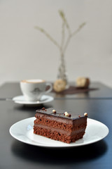 Chocolate cake on white plate with coffee in background