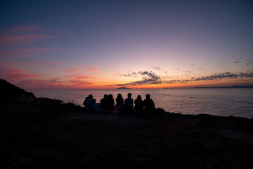 silhouette of a group of kids watching the sunset on the Sorrento coast with Ischia and Procida in background. Naples, Campania, Italy.
