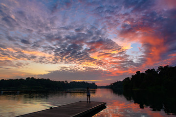 Alone women take sunset photo on wooden dock at peaceful lake