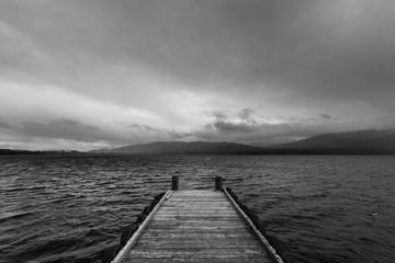 wooden dock in the lake with raining at mountain background, black and white
