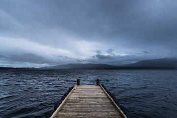 wooden dock in the lake with raining at mountain background