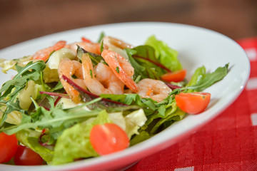 Vegetable salad with shrimp on white plate on red-white tablecloth