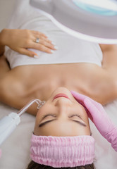 Girl receiving darsonval procedure electric massage at beauty salon. Hardware cosmetology. Selective focus.