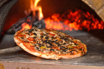 Pizza on the edge of a pizza oven with a burning fire in the background