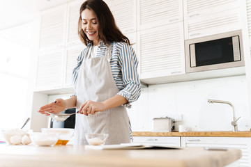 Image of cheerful brunette woman preparing dough while cooking pie