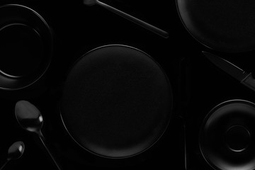 black kitchen items on a black background plates forks spoons knives with empty space in the middle