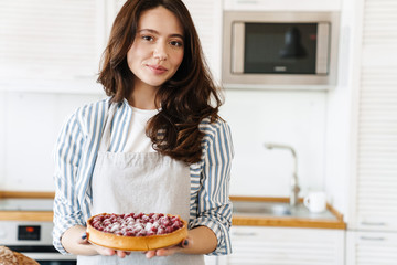 Image of pleased beautiful woman smiling and showing pie with raspberries