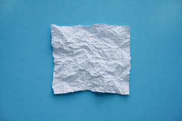 Crumpled square white checkered paper sheet on blue background top view