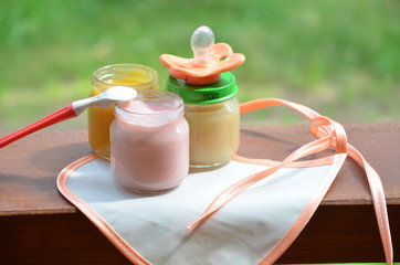 Baby food in jars puree mashed food on a background of foliage, With a pacifier and spoon