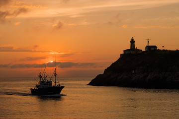Hermoso atardecer sobre la ría con la silueta del faro sobre la montaña con colores cálidos en...