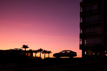 Fototapeta na wymiar Silueta de un coche junto a un edificio y las palmeras en una tarde de verano al ocaso con colores vivos