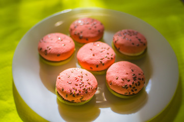 Multi-colored green and pink, bright cookies with two halves dressed with filling and sprinkled with sesame seeds on a white plate and on a bright salad background.