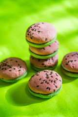Multi-colored green and pink, bright cookies with two halves dressed with filling and sprinkled with sesame seeds on a bright salad color background.