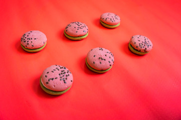 Multi-colored green and pink, bright cookies with two halves dressed with filling and sprinkled with sesame seeds on a bright pink color background.