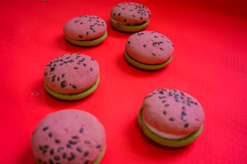 Fototapeta premium Multi-colored green and pink, bright cookies with two halves dressed with filling and sprinkled with sesame seeds on a bright pink color background.