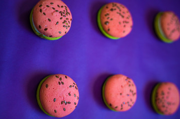 Multi-colored green and pink, bright cookies with two halves dressed with filling and sprinkled with sesame seeds on a bright blue color background.