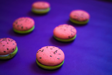 Multi-colored green and pink, bright cookies with two halves dressed with filling and sprinkled with sesame seeds on a bright blue color background.
