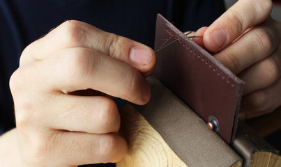 Working process in the leather workshop. Man is sewing wallet