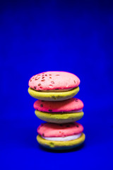 Multi-colored green and pink, bright cookies with two halves dressed with filling and sprinkled with sesame seeds on a bright blue color background.