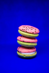 Multi-colored green and pink, bright cookies with two halves dressed with filling and sprinkled with sesame seeds on a bright blue color background.
