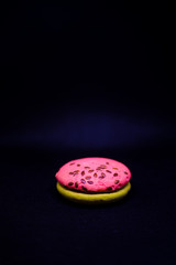 Multi-colored green and pink, bright cookies with two halves seasoned with filling and sprinkled with sesame seeds on a bright black color background.