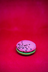 Multi-colored green and pink, bright cookies with two halves dressed with filling and sprinkled with sesame seeds on a bright red color background.