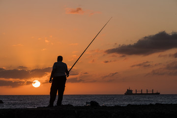 Pescador al atardecer un dia de verano pesca junto a la orilla