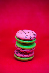 Multi-colored green and pink, bright cookies with two halves dressed with filling and sprinkled with sesame seeds on a bright red color background.