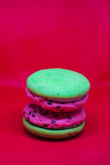 Multi-colored green and pink, bright cookies with two halves dressed with filling and sprinkled with sesame seeds on a bright red color background.
