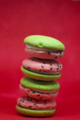 Multi-colored green and pink, bright cookies with two halves dressed with filling and sprinkled with sesame seeds on a bright red color background.