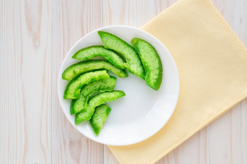 Green slices of succade of pomelo on white plate on wooden table. Candied citrus, confectionery...