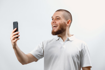 Portrait of a positive handsome bearded man in a white t-shirt talking on a video call using a smartphone