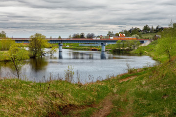 Fototapeta premium An automobile bridge over a small river surrounded by cottages and farm fields.
