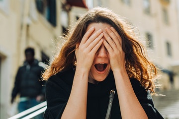 Fototapeta premium Close up headshot portrait of a young caucasian woman feeling stress, closing eyes with hands and open mouth. Human emotions, facial expression of fear, horror, scary, anxiety or phobia, 