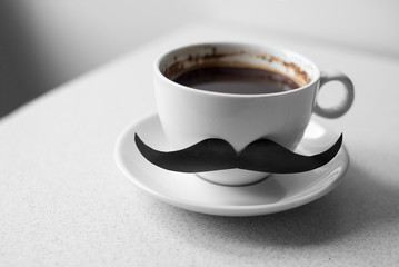 Closeup of a white ceramic cup with natural coffee drink by someone , with a fake mustache attached to it white background