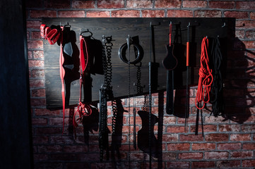 A set of varied leather lashes for sexual pleasures hang on a wooden hanger on a brick wall. Sex...