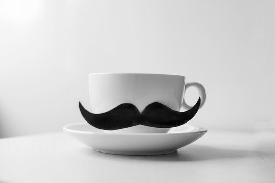 Closeup of a white ceramic cup coffee, with a fake mustache attached to it white background. Happy Father's Day concept. Place for text