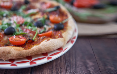 pizza with olives, cherry tomatoes and arugola on plate